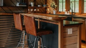 A rustic kitchen with wooden beams, a bar area with stools, and a window providing natural light.