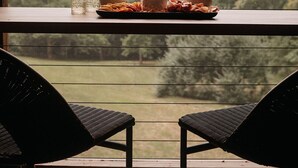 A balcony with a table set for two, overlooking a forested landscape.