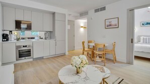 A modern kitchen with white cabinets, a built-in oven, and a dining area with a marble table and wooden chairs. - Vonder Miami Beach - Unit 3 (Miami Beach)