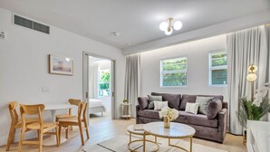 A modern living room with a grey sofa, wooden chairs, a round coffee table, and a white dining table. - Vonder Miami Beach - Unit 3 (Miami Beach)