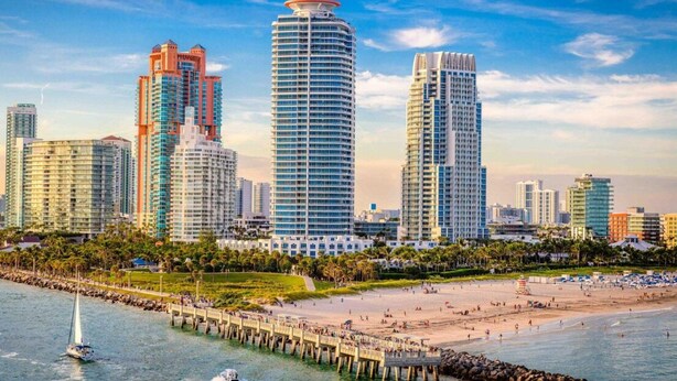 A coastal cityscape with high-rise buildings, a sandy beach, and a pier extending into the water. - Vonder Miami Beach - Unit 3 (Miami Beach)