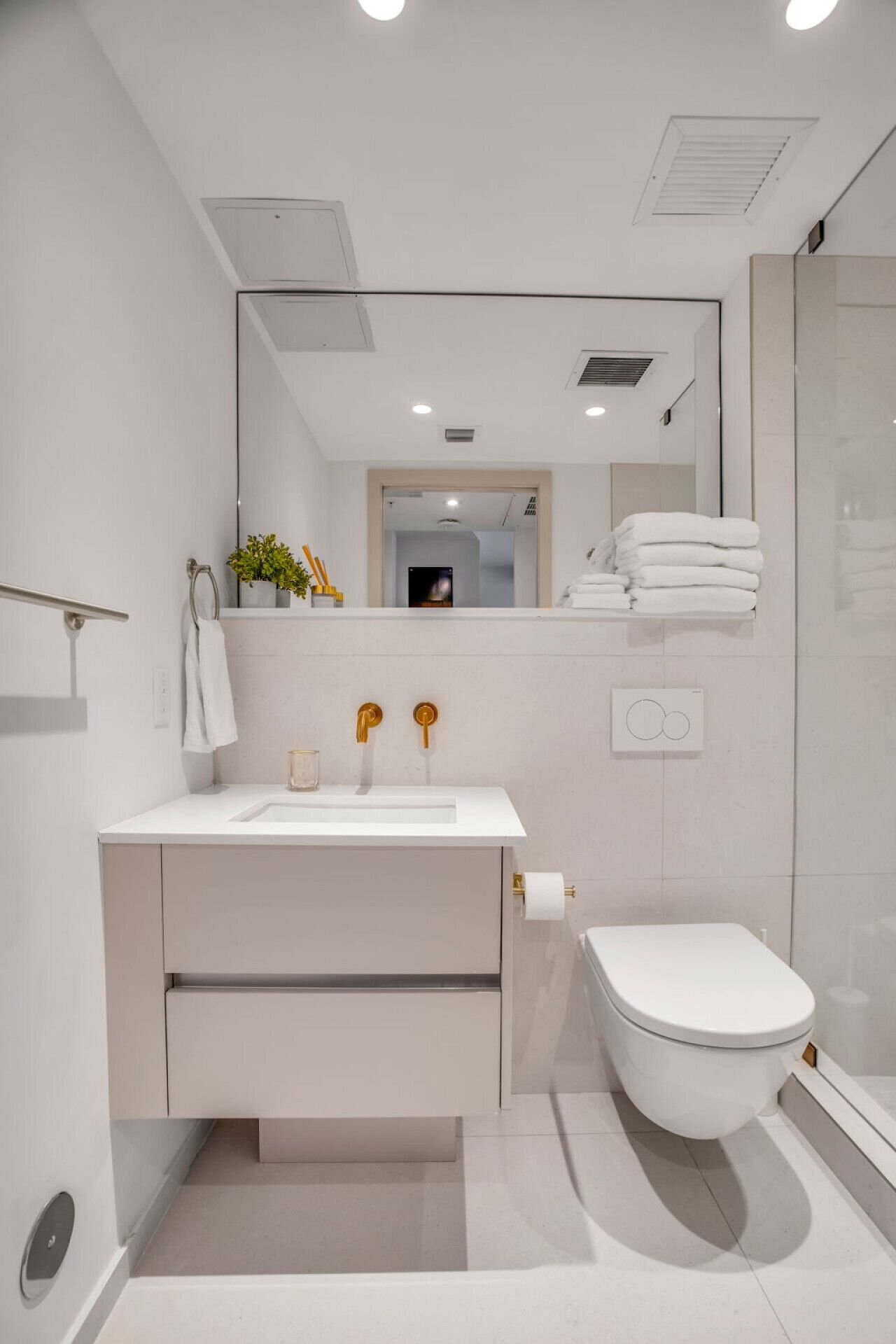 Une salle de bain moderne avec un lavabo blanc, des robinets dorés, des toilettes et une douche à parois de verre.