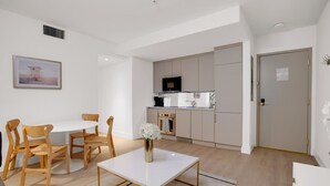 Une cuisine moderne équipée d’un four à micro-ondes, d’un four et d’un évier. On y trouve un coin repas avec une table blanche et des chaises en bois. Un tableau encadré est accroché au mur.