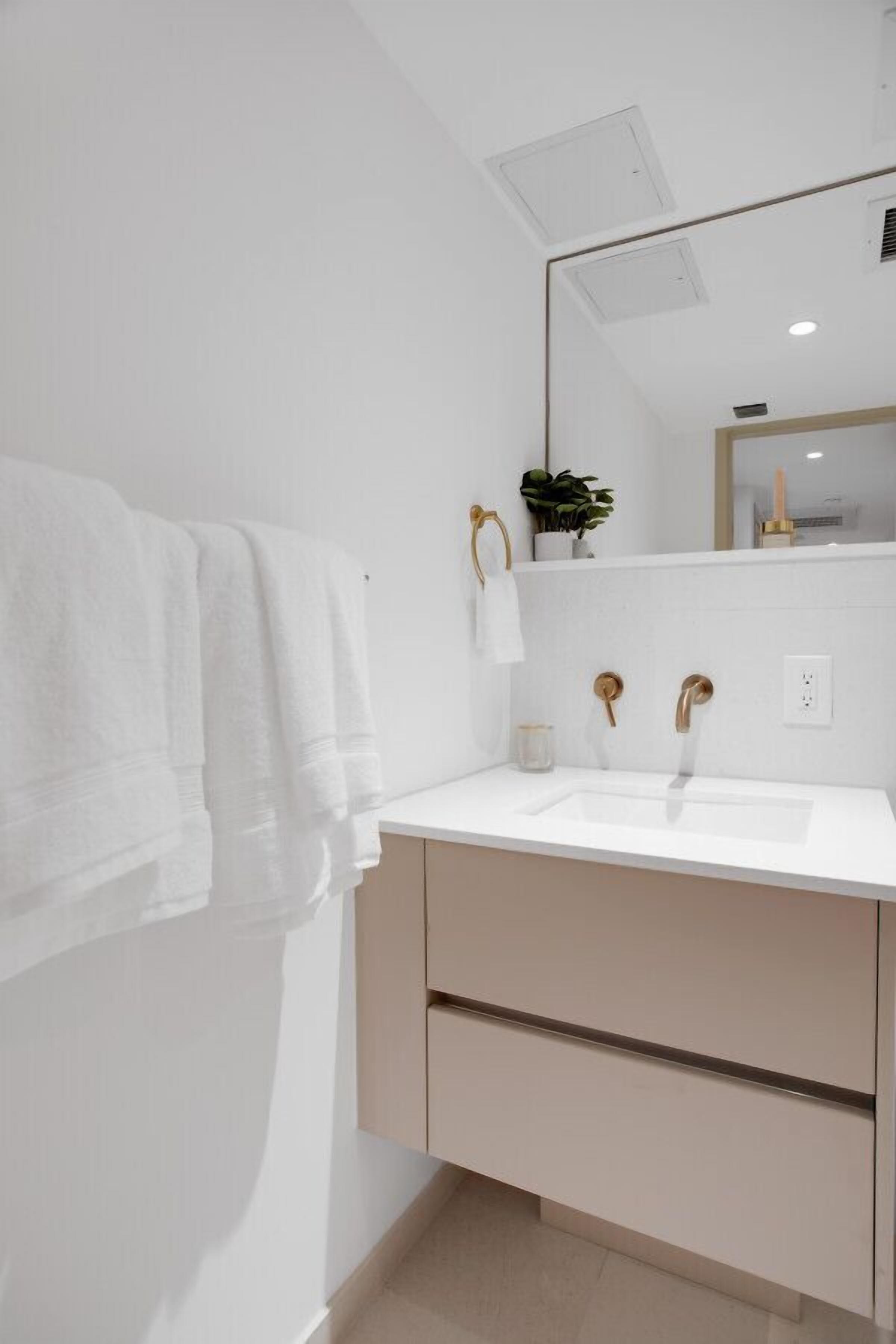 Une salle de bain moderne avec un lavabo blanc, des accessoires dorés et un miroir au-dessus.