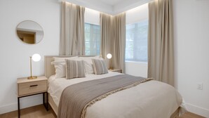 Une chambre moderne avec un grand lit, deux tables de chevet, un miroir rond et une fenêtre avec des rideaux.