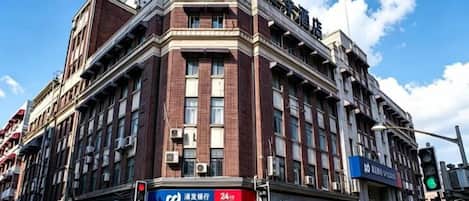 Un edificio de varios pisos con una entrada destacada en la esquina, un letrero de banco a la vista y un semáforo.