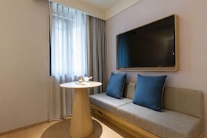 A hotel room with a sofa, a round table, a flat-screen TV, and a window with curtains. - JI Hotel (Shanghai The Bund Ningbo Road) (Shanghai)
