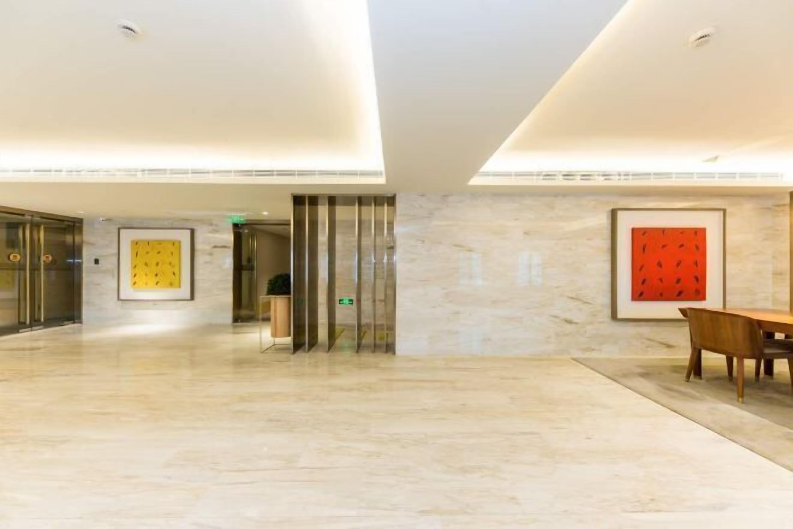 Eine großzügige Lobby mit Marmorboden, einem Holztisch und gerahmten Kunstwerken an den Wänden.