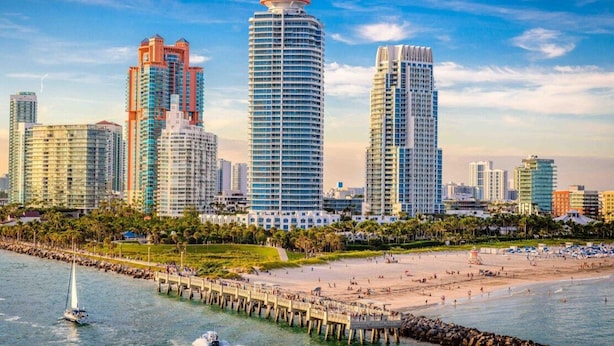 A coastal cityscape with high-rise buildings, a sandy beach, and a pier extending into the water. - Vonder Miami Beach - Unit 12 (Miami Beach)