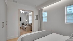 A modern bedroom with a large bed, a sofa in the adjacent living area, and a view of the outdoors through a window. - Vonder Miami Beach - Unit 12 (Miami Beach)