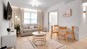 A modern living room with a sofa, round coffee table, and wooden chairs. - Vonder Miami Beach - Unit 12 (Miami Beach)