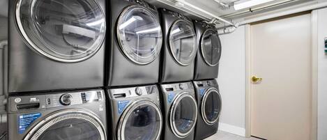 A row of four stacked front-loading washing machines in a commercial laundry room.