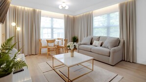 Un salon moderne avec un canapé beige, une table basse blanche et un coin repas doté de chaises en bois.