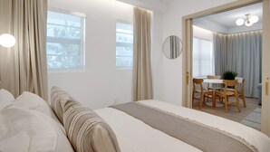 Une chambre d’hôtel moderne dotée d’un grand lit, d’un coin repas avec une table et des chaises, et offrant une vue sur l’extérieur grâce à de grandes fenêtres.
