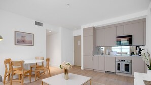 A modern kitchen with built-in appliances, a dining area with wooden chairs, and a white table. - Vonder Miami Beach - Unit 16 (Miami Beach)