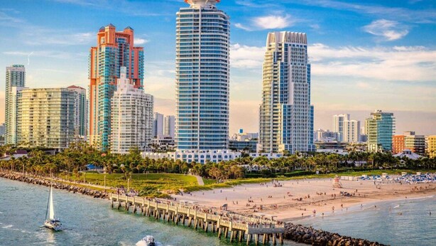 A coastal cityscape with high-rise buildings, a sandy beach, and a pier extending into the water. - Vonder Miami Beach - Unit 16 (Miami Beach)