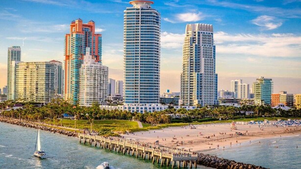 A coastal cityscape with high-rise buildings, a sandy beach, and a pier extending into the water. - Vonder Miami Beach - Unit 18 (Miami Beach)
