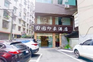 Un bâtiment sur lequel on peut lire l’inscription « 田国印豪酒店 » et un parking où sont garées plusieurs voitures.