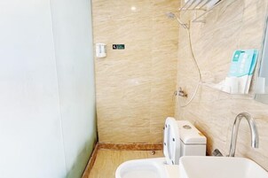 Baño pequeño con inodoro, lavamanos y ducha. Hay un perchero y un dispensador de jabón en la pared.