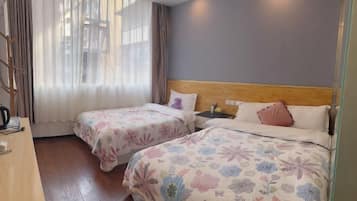 A hotel room with two beds, a wooden headboard, a desk with a chair, and a window with sheer curtains.