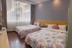 Habitación de hotel con dos camas, cabecero de madera, un escritorio con silla y una ventana con cortinas ligeras.