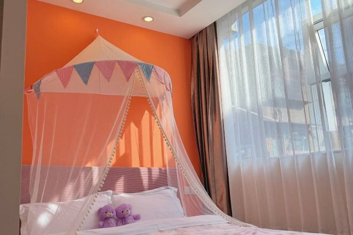 Una cama con dosel, un oso de peluche y una ventana con cortinas.