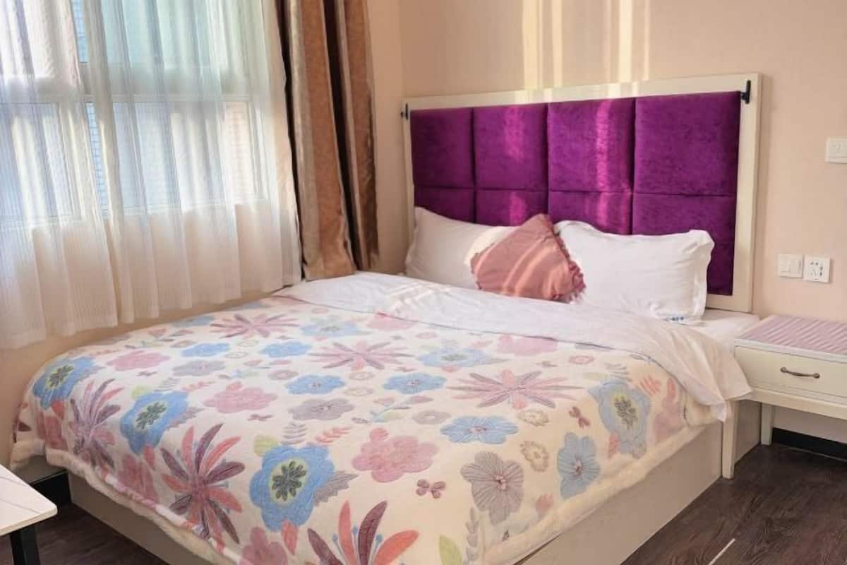 Un dormitorio con cama, mesita de noche y ventana con cortinas.