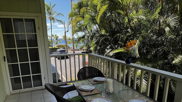 A dining area with a glass table set for four, surrounded by wicker chairs with green cushions.