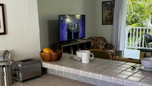 A kitchen with a tiled countertop, a toaster, a bowl of fruit, a coffee maker, and a television displaying a nature scene.