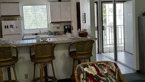 A kitchen with a bar area, white cabinets, a refrigerator, and a window.