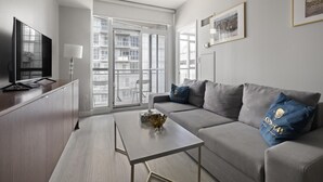 A modern living room with a grey sofa, a coffee table, and a TV on a wooden cabinet. - GLOBALSTAY. High Floor in Downtown Toronto 1bd+den (Toronto/Canada)