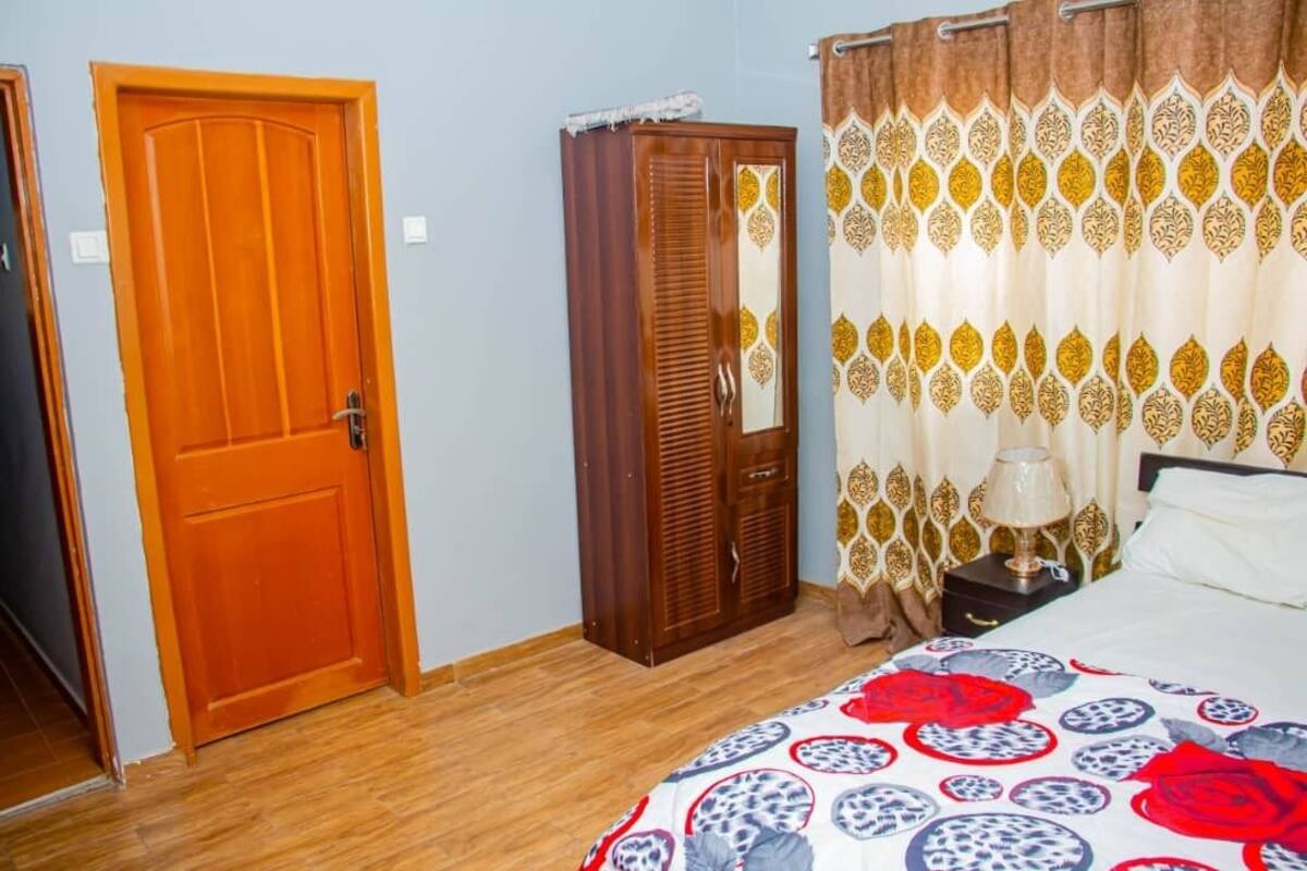 Una camera da letto con una porta in legno, un armadio, un letto con copriletto decorato e tende a motivo geometrico.