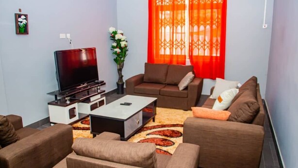 A living room with a flat-screen TV, brown sofas, a coffee table, and a decorative rug. - Accra Cosy Homes (Ngleshi Amanfro)