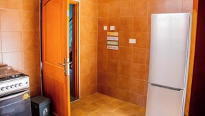 A kitchen with orange tiles, a white refrigerator, a stove, and a door leading to a closet. - Accra Cosy Homes (Ngleshi Amanfro)