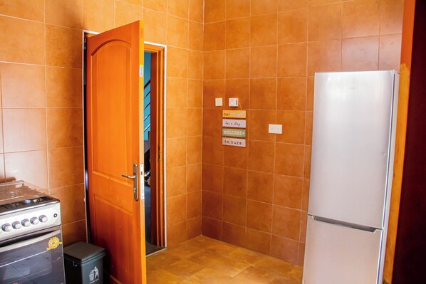 A kitchen with orange tiles, a white refrigerator, a stove, and a door leading to a closet. - Accra Cosy Homes (Ngleshi Amanfro)