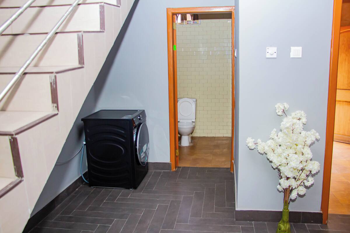Corridoio di un albergo con una lavatrice, un gabinetto e un vaso con fiori.