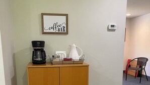 Ett litet pentry med en kaffebryggare, en vattenkokare och en skylt med texten ”kafé” på väggen.