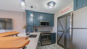 A modern kitchen with teal cabinets, a stainless steel refrigerator, a microwave, and a tiled backsplash. - Charming 1-bedroom waterfront condo in fabulous Spring Lake. (Spring Lake)