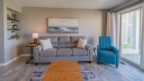 A living room with a grey sofa, a blue armchair, a wooden coffee table, a lamp, and a painting on the wall. - Charming 1-bedroom waterfront condo in fabulous Spring Lake. (Spring Lake)
