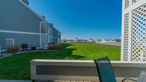 A patio with a view of a well-maintained lawn and a building with a lattice window. - Charming 1-bedroom waterfront condo in fabulous Spring Lake. (Spring Lake)