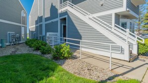 A modern building with a staircase leading to the entrance, surrounded by a well-maintained lawn and gravel path. - Charming 1-bedroom waterfront condo in fabulous Spring Lake. (Spring Lake)