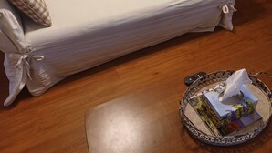 Un soggiorno con un divano bianco, una sveglia, un'area pranzo con tavolo e sedie, e una cucina sullo sfondo.
