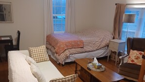 Un accogliente soggiorno con un divano, un letto con lenzuola a righe, un tavolino in legno e un piccolo tavolino di servizio.