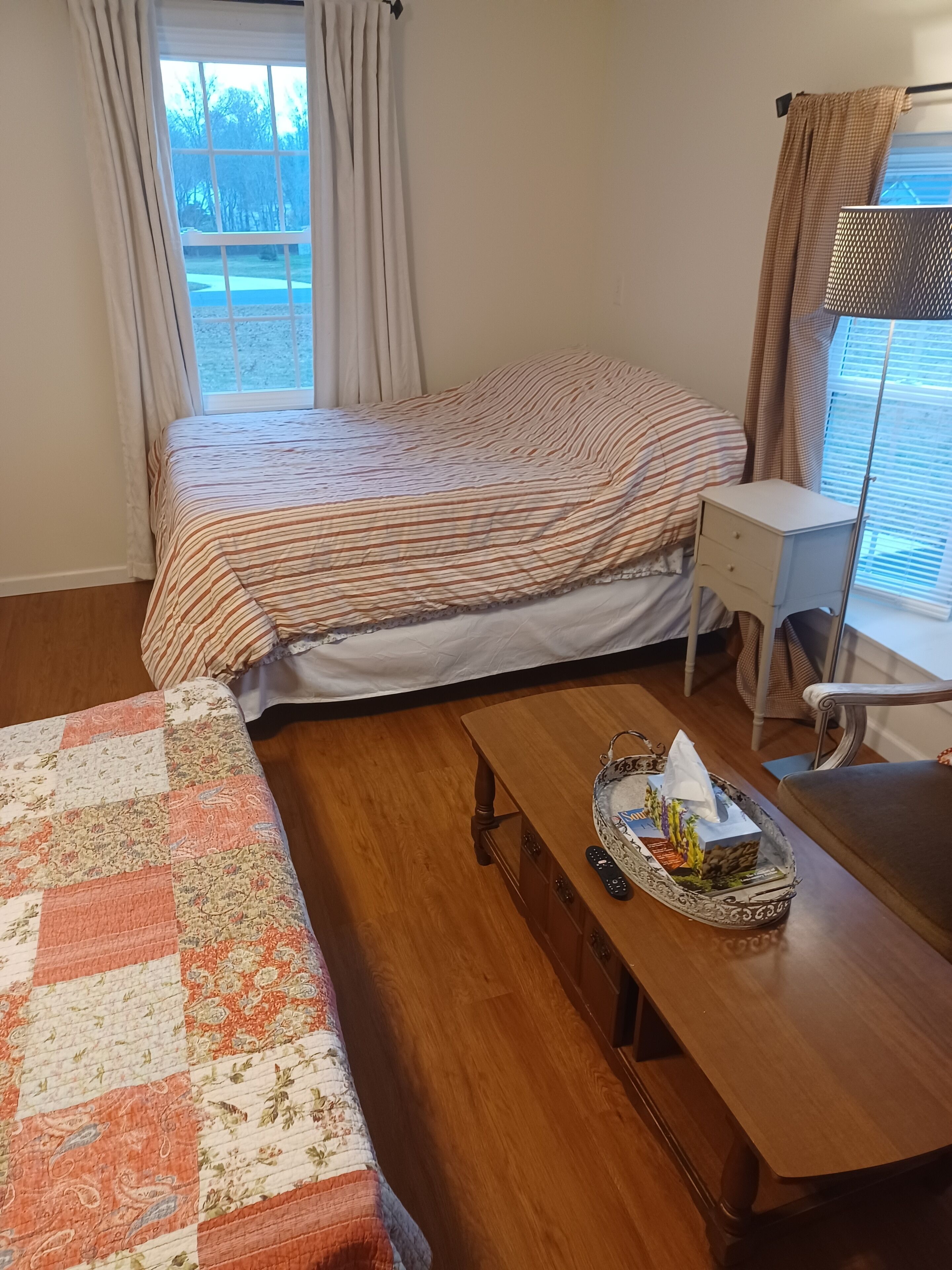 Un dormitorio con cama, escritorio, silla y piso de madera.