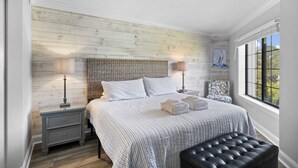 Camera da letto con parete in legno, un letto con copripiumino a righe, due comodini con lampade, una panca e una finestra con vista.