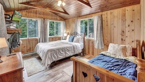Une chambre dans une cabane en bois, avec deux lits, un bureau et un ventilateur.
