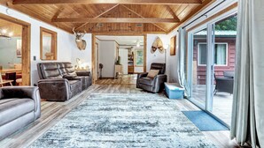 Un vaste salon doté d’un plafond en bois, de canapés en cuir, d’un tapis à motifs et d’une grande porte-fenêtre coulissante donnant sur un espace extérieur.