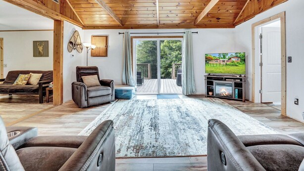 Un vaste salon doté d’un plafond en bois, d’une cheminée, d’un téléviseur et d’une grande fenêtre donnant sur une maison.