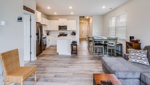 A modern kitchen with white cabinets, a central island, and a dining area with a gray sofa and a coffee table.