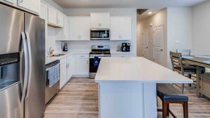 A modern kitchen with white cabinets, stainless steel appliances, a central island, and a dining area with a table and chairs.